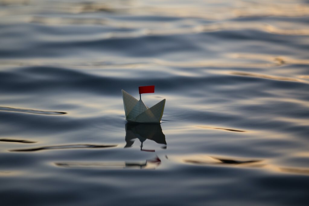 Papierschiffchen mit roter Fahne auf Wasser